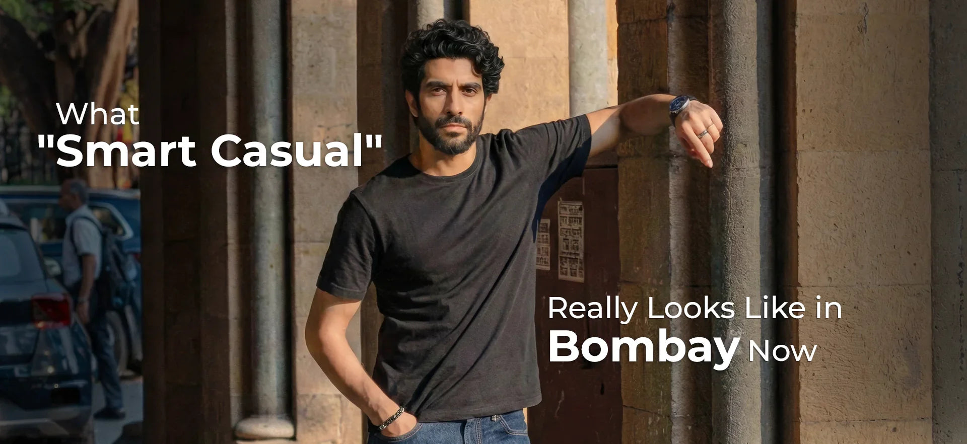 Smart casuals: Man in a black tee and denim jeans leaning against a stone pillar in Bombay
